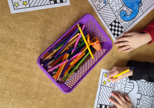 Dzieci kolorują obrazek przedstawiający dinozaura.