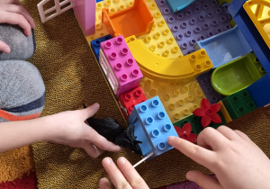 Dzieci bawią się dinozaurami w zbudowanym przez siebie świecie z klocków.