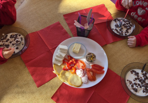 Dzieci jedzą śniadanie, na stole czerwone serwetki.