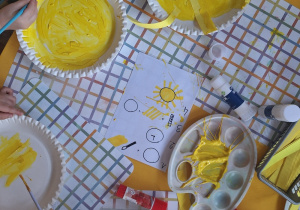 Dzieci malują żółtą farbą papierowe talerzyki.