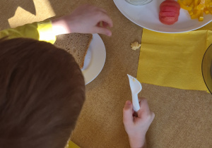 Chłopiec ubrany na żółty siedzi przy stole podczas posiłku.