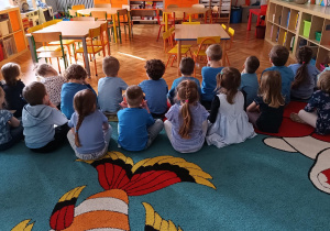 Na dywanie siedzą dzieci ubrane na niebiesko.