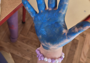 Dziecko pokazuje dłoń pomalowaną niebieską farbą.
