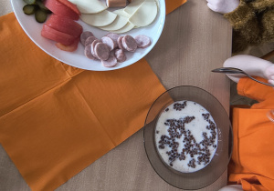 Dzieci jedzą śniadanie, na stole pomarańczowe serwetki.