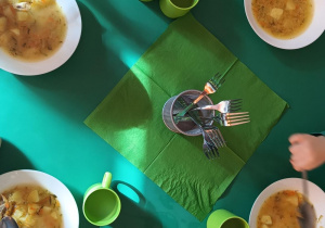 Dzieci jedzą zupę, na stole zielone serwetki.