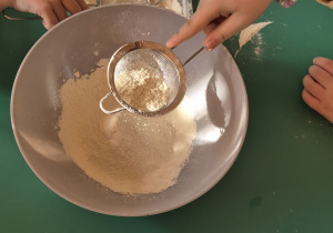 Dzieci przesiewają mąkę do miski.