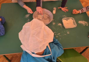 Przedszkolaki przy stoliku przesiewają mąkę.