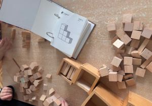 Dzieci przy stoliku układają drewniane  klocki - dary Froebla wg wzorów.