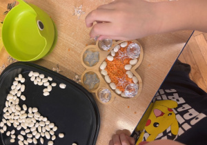 Dziecko układa wysypywanke w kształcie łapki psa z soczewicy, fasoli i koralików.