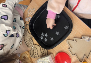 Dziecko na stoliku, na czarnej tacy układa gwiazdki.