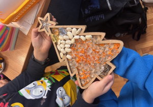 Dziecko prezentuje wysypywankę, choinkę z soczewicy, fasoli, koralików gwiazdek.