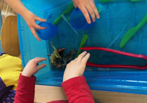 Dzieci przelewają wodę w niebieskim pojemniku.