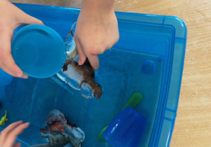 Dziecko polewa wodą dinozaura w lodzie.