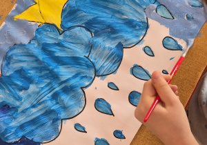 Dziecko przy stoliku maluje z wykorzystaniem farb marcową pogodę.