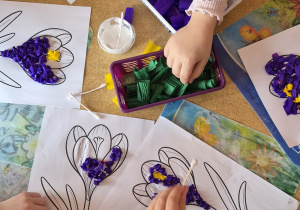 Dzieci z wykorzystaniem kuleczek z fioletowej bibuły wyklejają szablon krokusa.