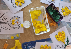 Dzieci z wykorzystaniem kuleczek z żółtej bibuły wyklejają szablon krokusa.