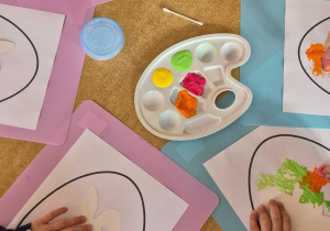 Dzieci z wykorzystaniem gąbki stemplują kontur jajka, na środku jajka szablon zajączka.