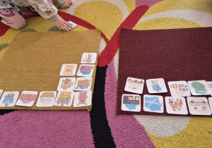 Dziewczynka bierze obrazek z dywanu - przed nią dwa dywaniki na których ułożone elementy charakterystyczne dla miasta oraz dla wsi.