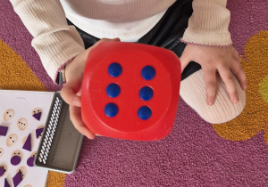 Dziewczynka w ręce trzyma dużą kostkę do gry.