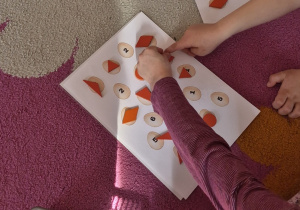 Dzieci układają dary zabawy Froebla na karcie pracy, na której znajdują się jajka oznaczone różnymi cyframi.