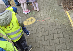 Dzieci ustawione w parach przed przedszkolem ubrane w odblaskowe kamizelki.