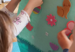 Dzieci przyczepiają elementy związane z Wielkanocą do dużej pisanki.