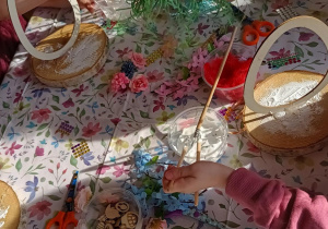 Dzieci wykonują stroiki - przyklejają jajko do drewnianej podstawki.