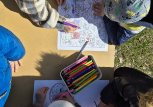 Dzieci w ogrodzie kolorują wielkanocny obrazek.