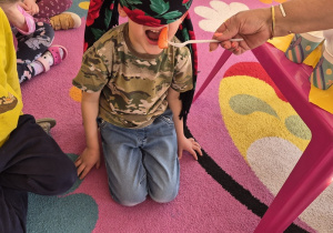 Chłopiec ma zasłonięte oczy i otwiera buzię - nauczyciel daje mu do spróbowania truskawkę.