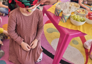 Dziewczynka ma zasłonięte oczy i otwiera buzię - nauczyciel daje jej do spróbowania winogrono.