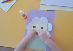 Dziewczynka przykleja czerwone usta z papieru na swoją pracę.
