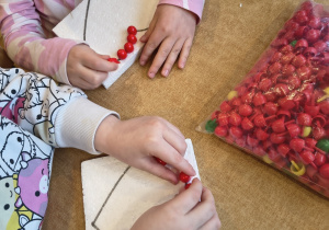 Dzieci wbijają czerwone pinezki w styropian, na którym narysowane jest serce.