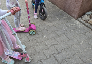 Dzieci jeżdżą na hulajnogach i rowerkach.