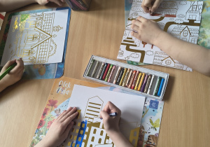 Dzieci kolorują kredkami miasto.