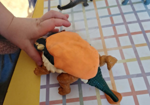 Dziecko odbija grzbiet dinozaura w pomarańczowej plastelinie.