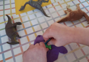 Dziecko odbija ślady dinozaura w fioletowej plastelinie.