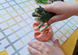 Dziecko odbija ślady T-rexa w pomarańczowej plastelinie.