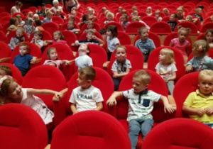 - Dzieci siedzą w czerwonych fotelach i czekają na przedstawienie