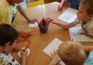 - Dzieci siedząc przy stoliku rysują kredkami kolorowe kropki