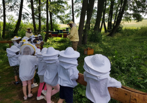Dzieci ubrane w strój pszczelarza, poznają zawód pszczelarza.