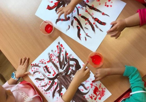 Dzieci malują na kartce farbami drzewa.