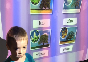 Chłopiec prezentuje pory roku przy tablicy multimedialnej.