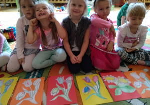 Dzieci prezentują swoje prace na dywanie.