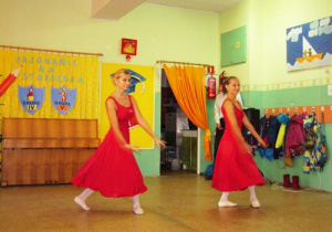 Dwie kobiety tańczą w długich czerwonych sukienkach.