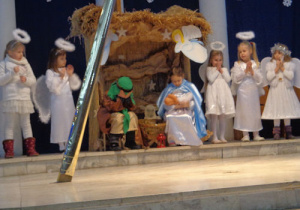 Józef z Maryją w szopce. Obok nich stoją dzieci w strojach aniołków.