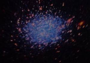 Galaktyka – skupisko wielu świecących punktów w odcieniach pomarańczowego i błękitnego.