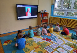 Dzieci siedzą przed tablicą multimedialną.