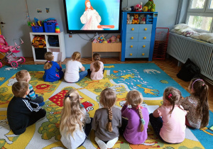 Dzieci siedzą przed monitorem interaktywnym i oglądają bajkę.