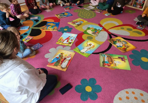Dzieci siedzą w kole na dywanie, a przed nimi leżą rozłożone obrazki.