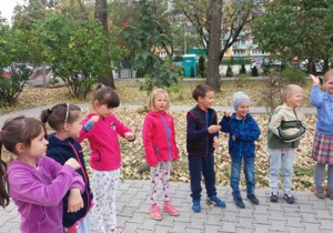 Uśmiechnięte dzieci stoją na ścieżce w przedszkolnym ogrodzie.
